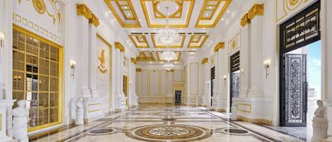 A grand hallway with marble floors, gold accents, and chandeliers.