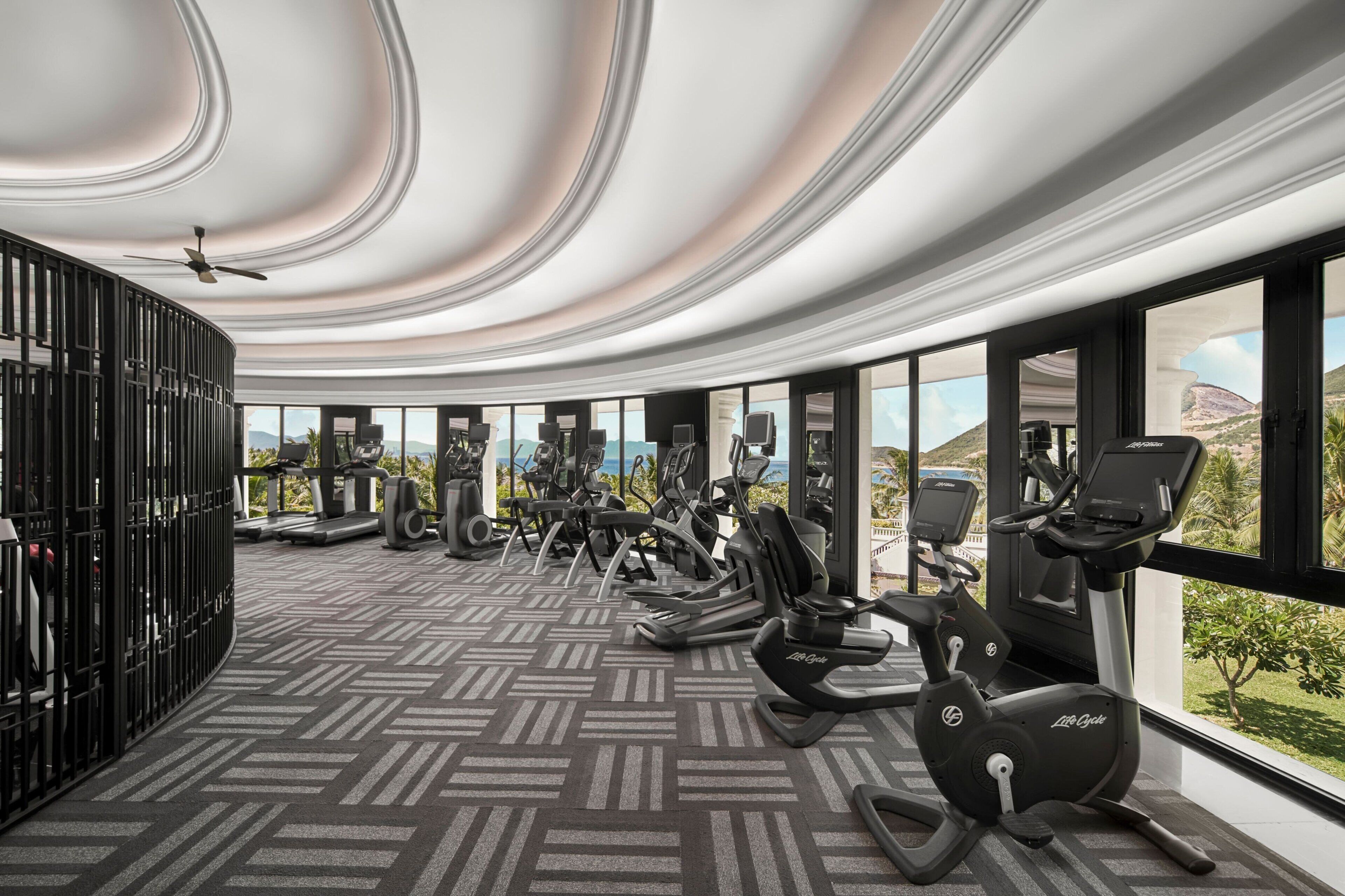 A modern gym with exercise equipment and large windows offering a view of the outdoors.