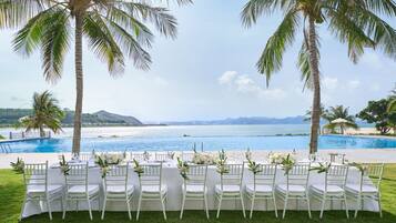 A table set up for a wedding with white chairs and floral centerpieces, overlooking a pool and a scenic view of the ocean.