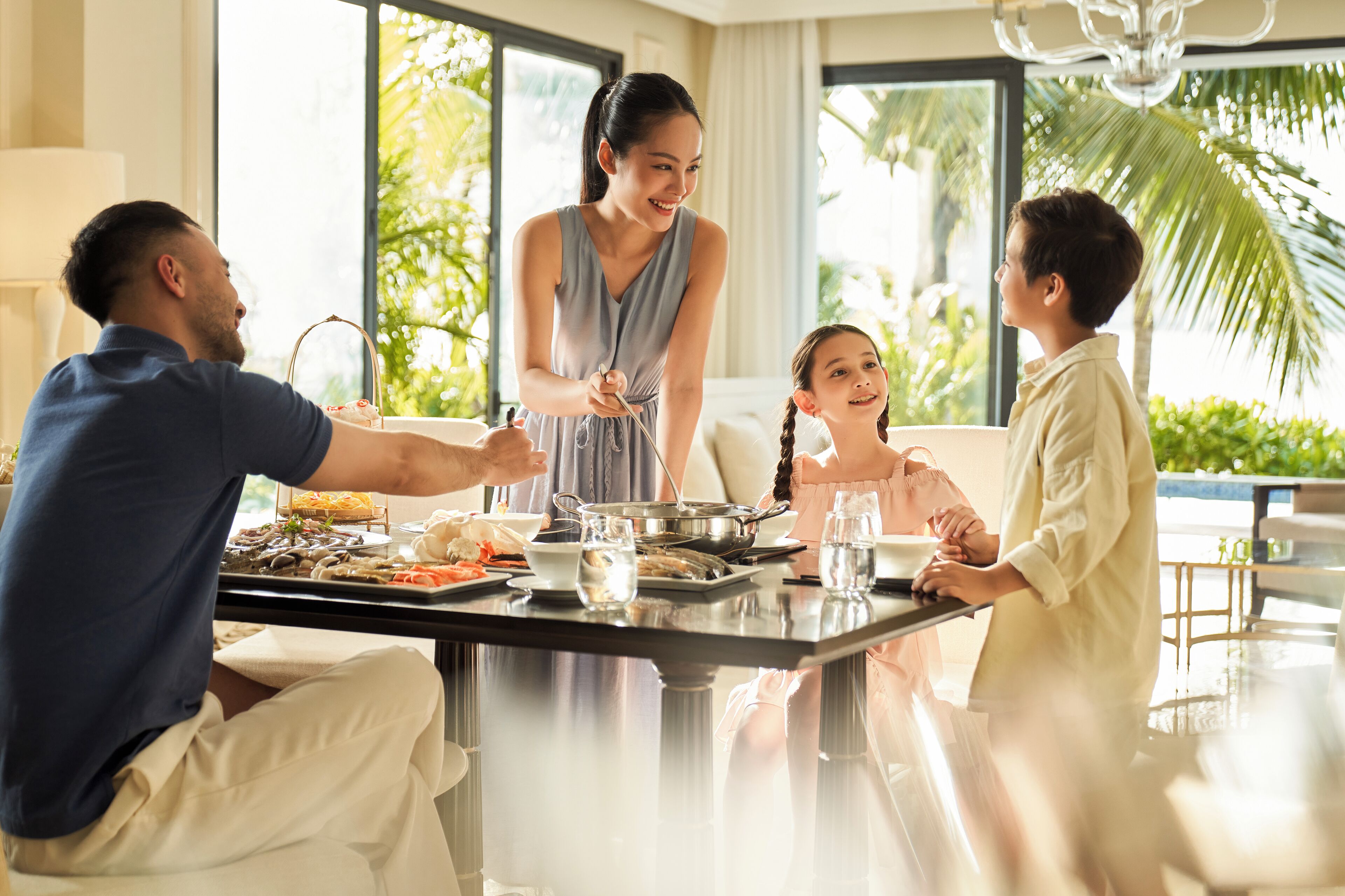A family dining at a table with a variety of dishes, in a room with large windows and a view of greenery.