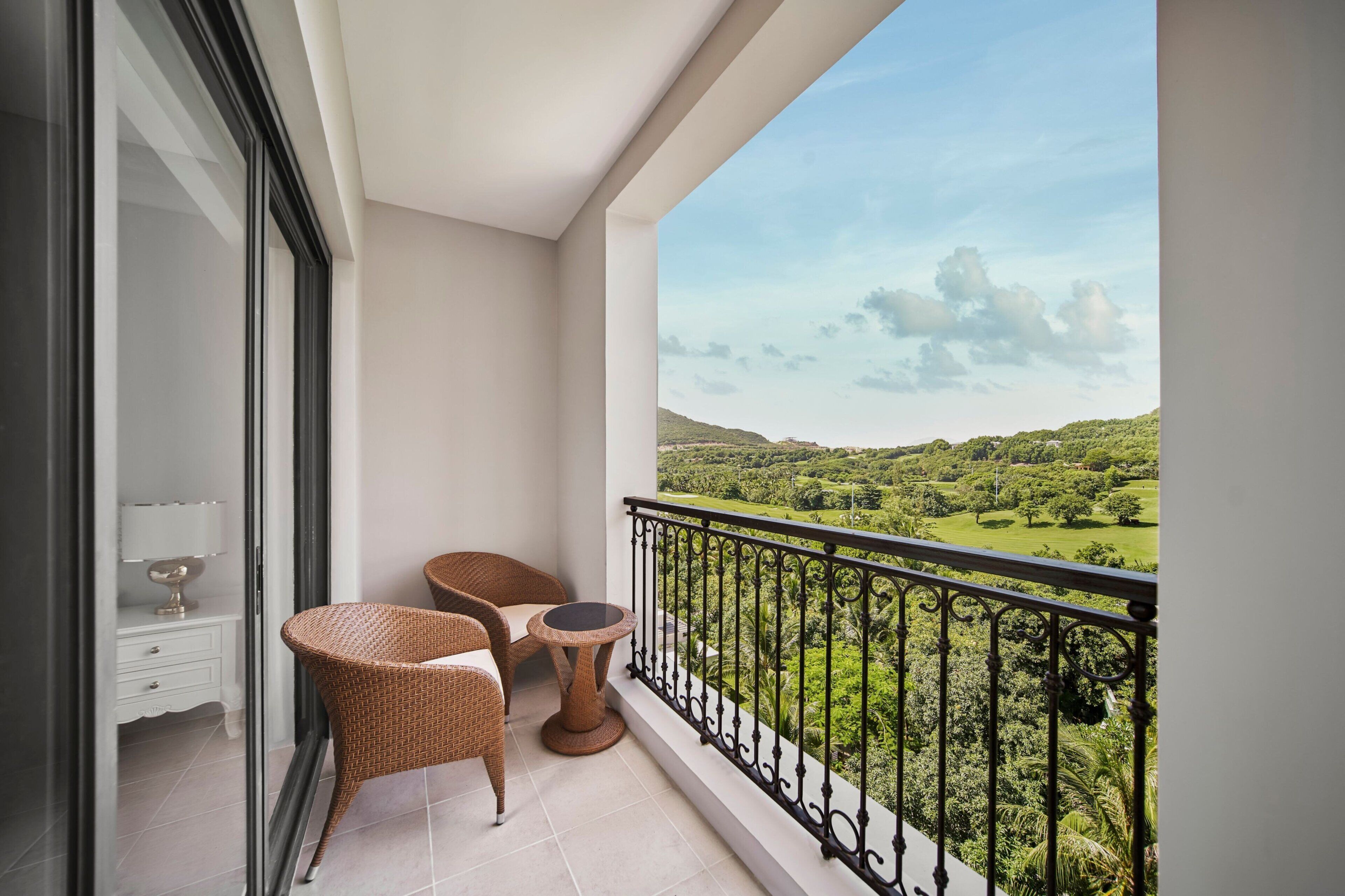 A balcony with wicker furniture, a small table, and a view of a green landscape.