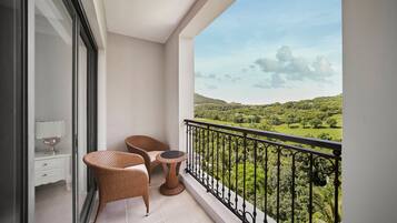 A balcony with wicker furniture, a small table, and a view of a green landscape.