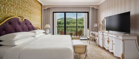 A luxurious hotel room with a large bed, a television, a balcony with a scenic view, and elegant decor.