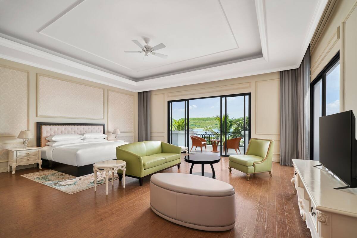 Una habitación de hotel con una cama grande, un sofá verde, una mesa redonda y un televisor.