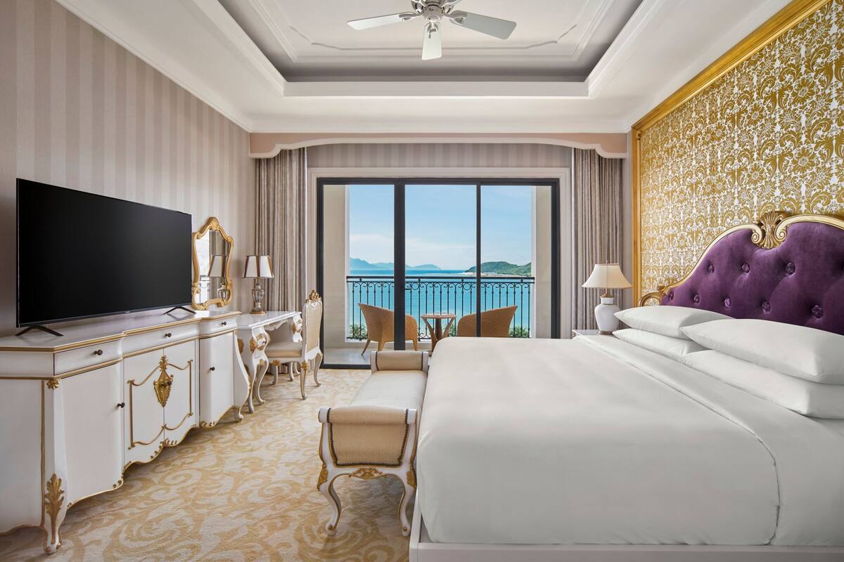 Una lujosa habitación de hotel con una cama grande, un televisor, un escritorio con una silla y un balcón con vista al mar.