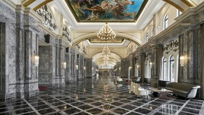 Un vaste hall d’entrée avec un sol en marbre, des colonnes de style classique, un grand lustre et une fresque au plafond.