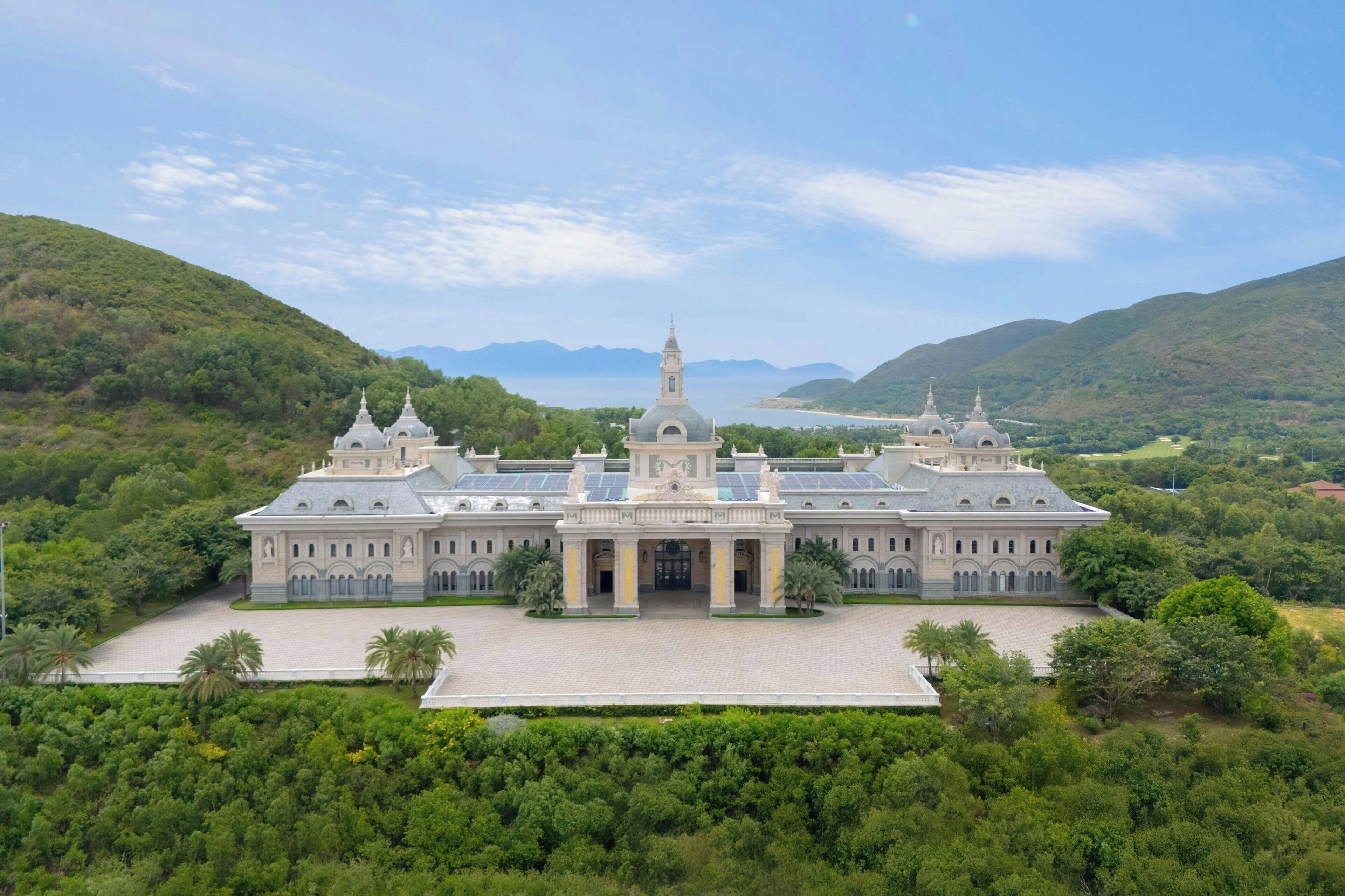 A large, historic building with a central dome and two symmetrical towers, surrounded by lush greenery and hills.