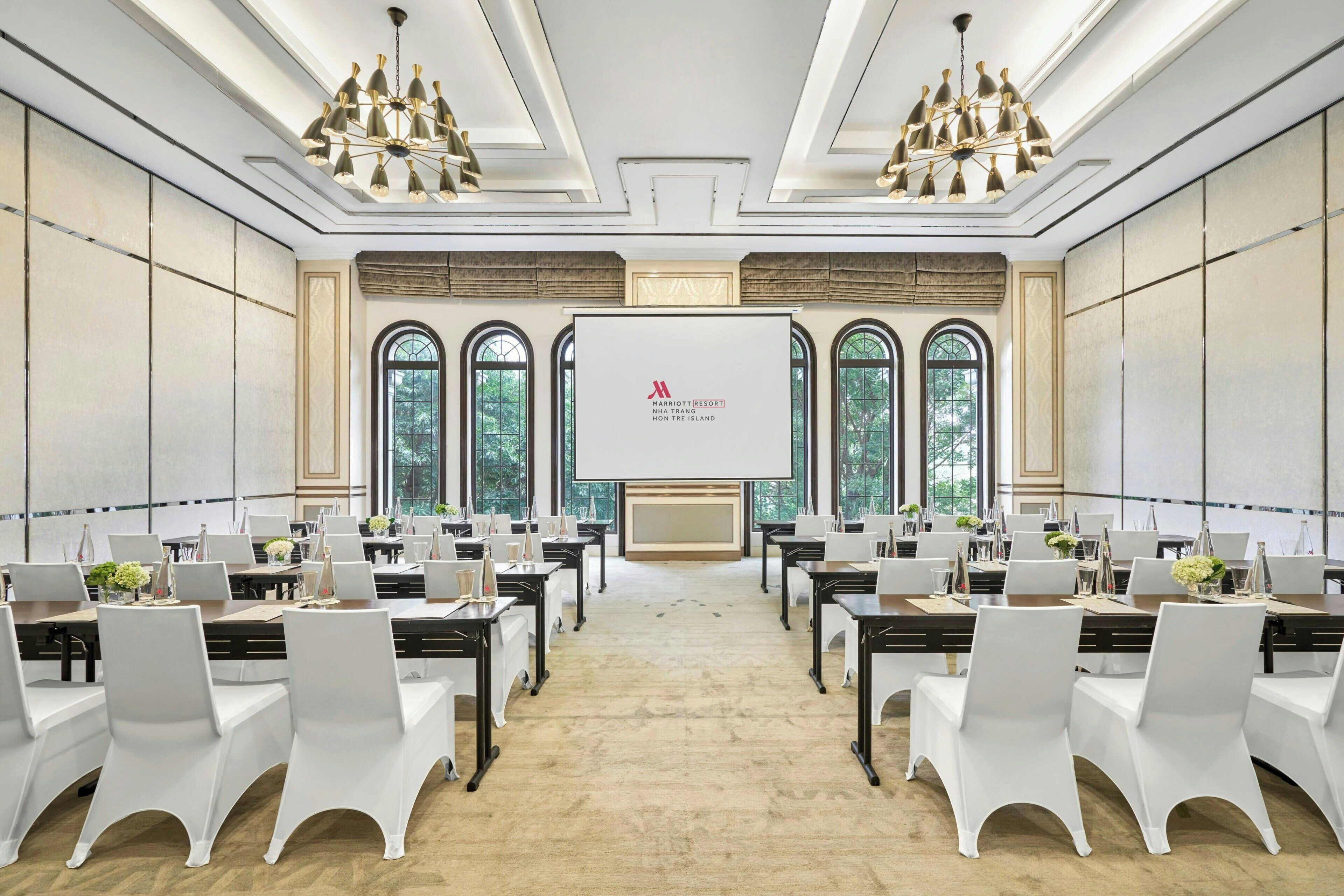 A conference room with a large screen, white chairs, and tables arranged for a meeting.