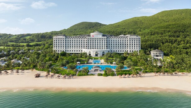 Un grand hôtel de villégiature doté d’une piscine centrale, entouré d’une végétation luxuriante et donnant sur une plage.