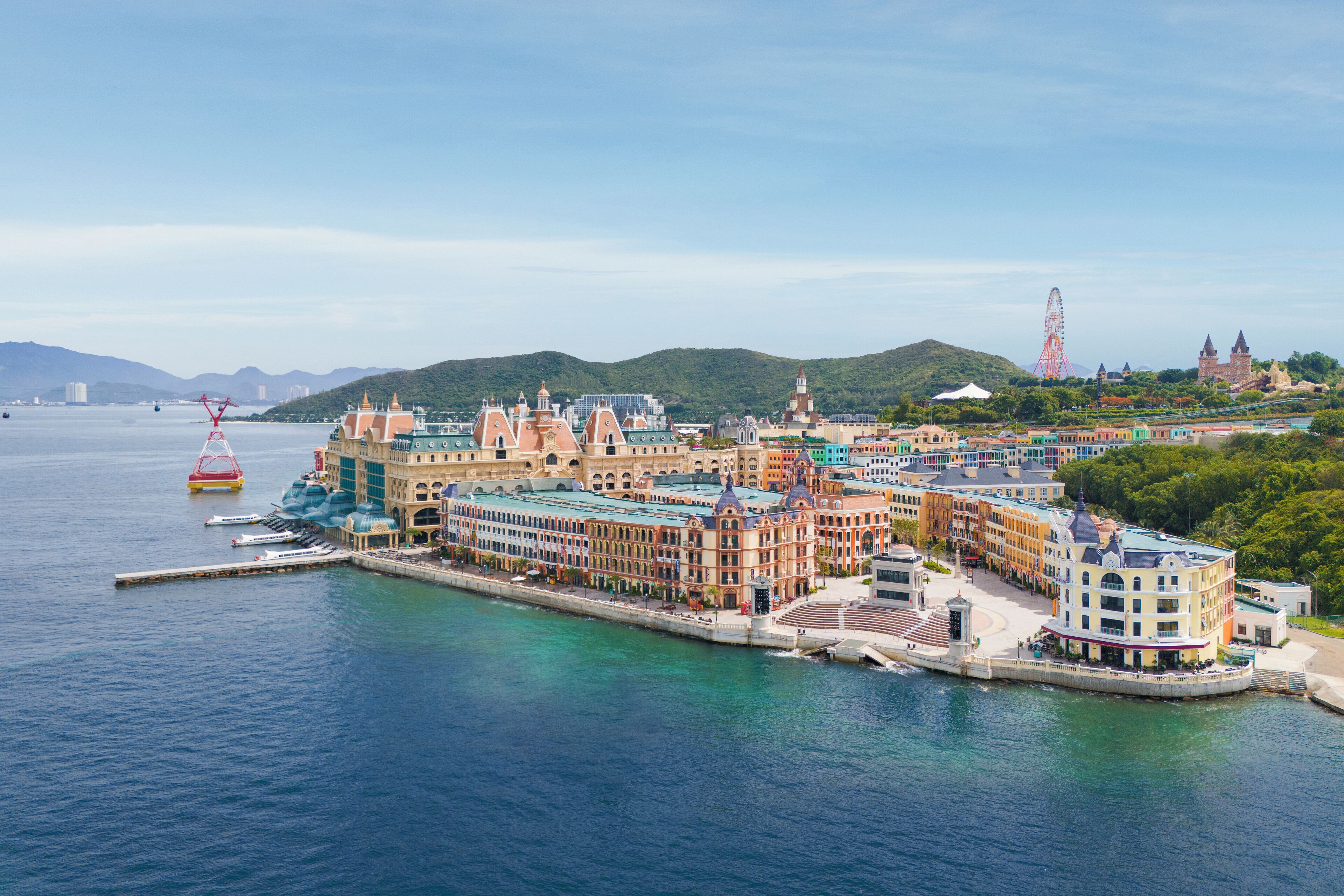 A waterfront hotel with multiple buildings, a pier, and a Ferris wheel in the background.