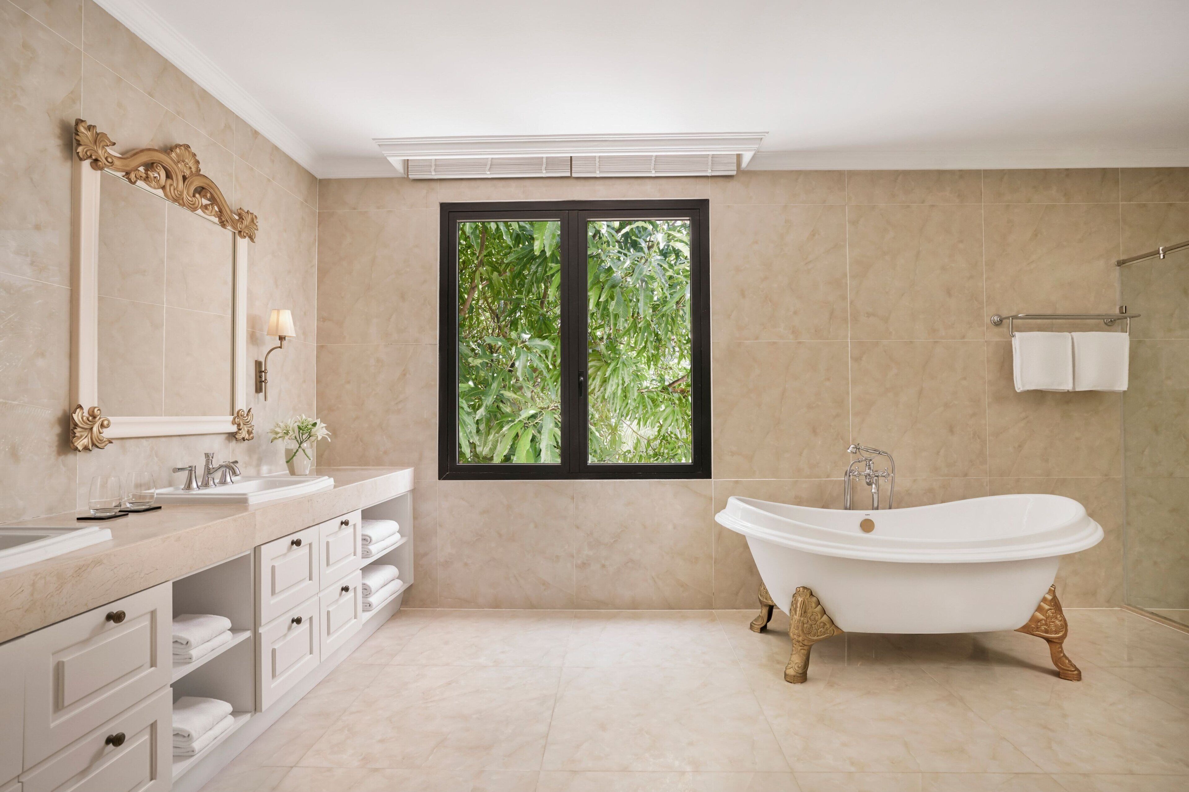 Une salle de bain avec une baignoire, un grand miroir et une fenêtre donnant sur un paysage verdoyant.