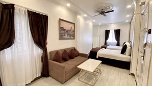 Une chambre d’hôtel moderne équipée d’un canapé, de deux lits simples, d’une petite table et d’un ventilateur de plafond.