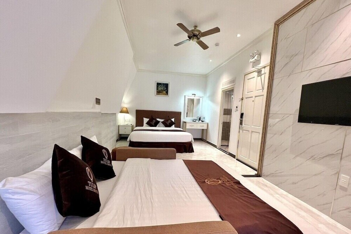 A hotel room with two beds, a ceiling fan, a bathroom with a mirror, and a wardrobe.