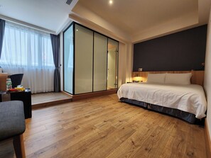 A hotel room with a bed, a desk, a chair, a wardrobe, and a large window with curtains. - Grange Inn (Taitung)