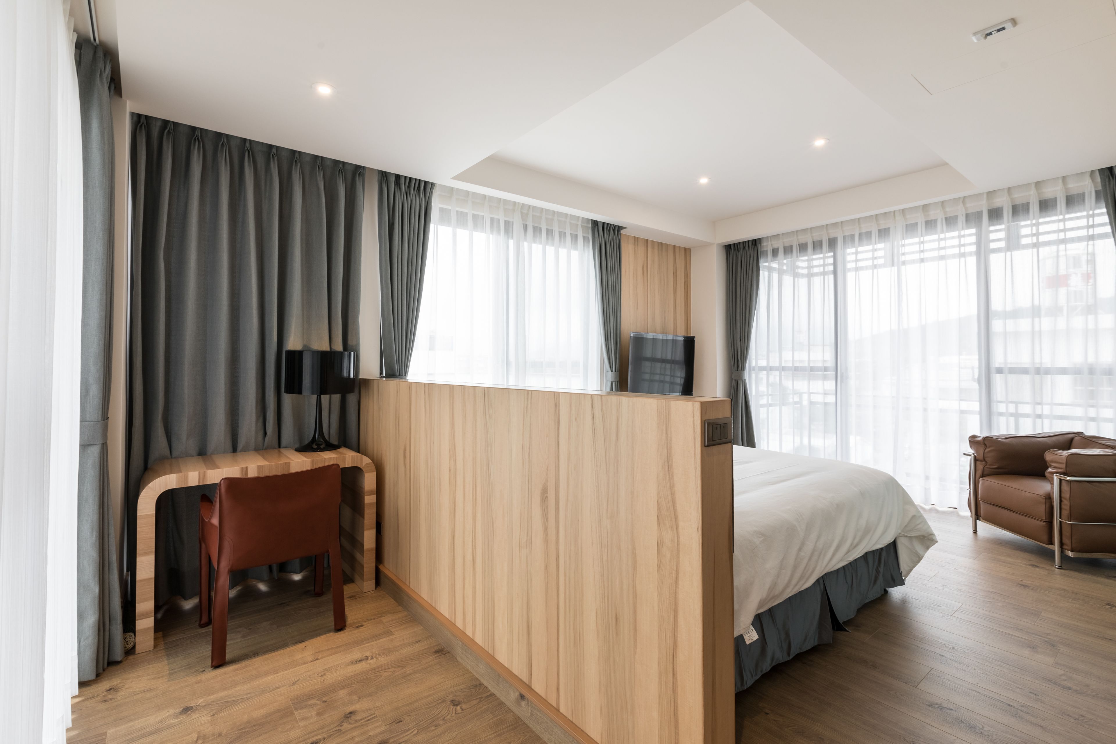 A modern hotel room with a wooden desk, a bed, and a sofa.