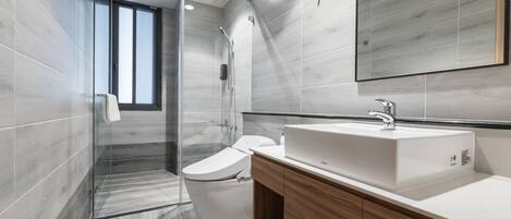 Un baño moderno con cabina de ducha de vidrio, inodoro blanco y tocador de madera con lavabo.
