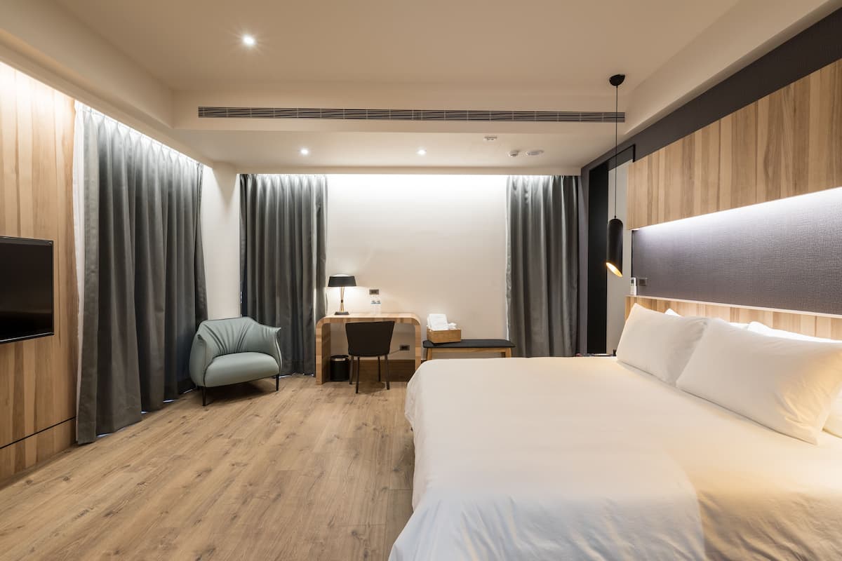 A modern hotel room with a large bed, a desk with a chair, a flat-screen TV, and wooden paneling.
