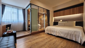 Una habitación de hotel moderna con una cama grande, una zona de estar, cabina de ducha de vidrio y suelo de madera.