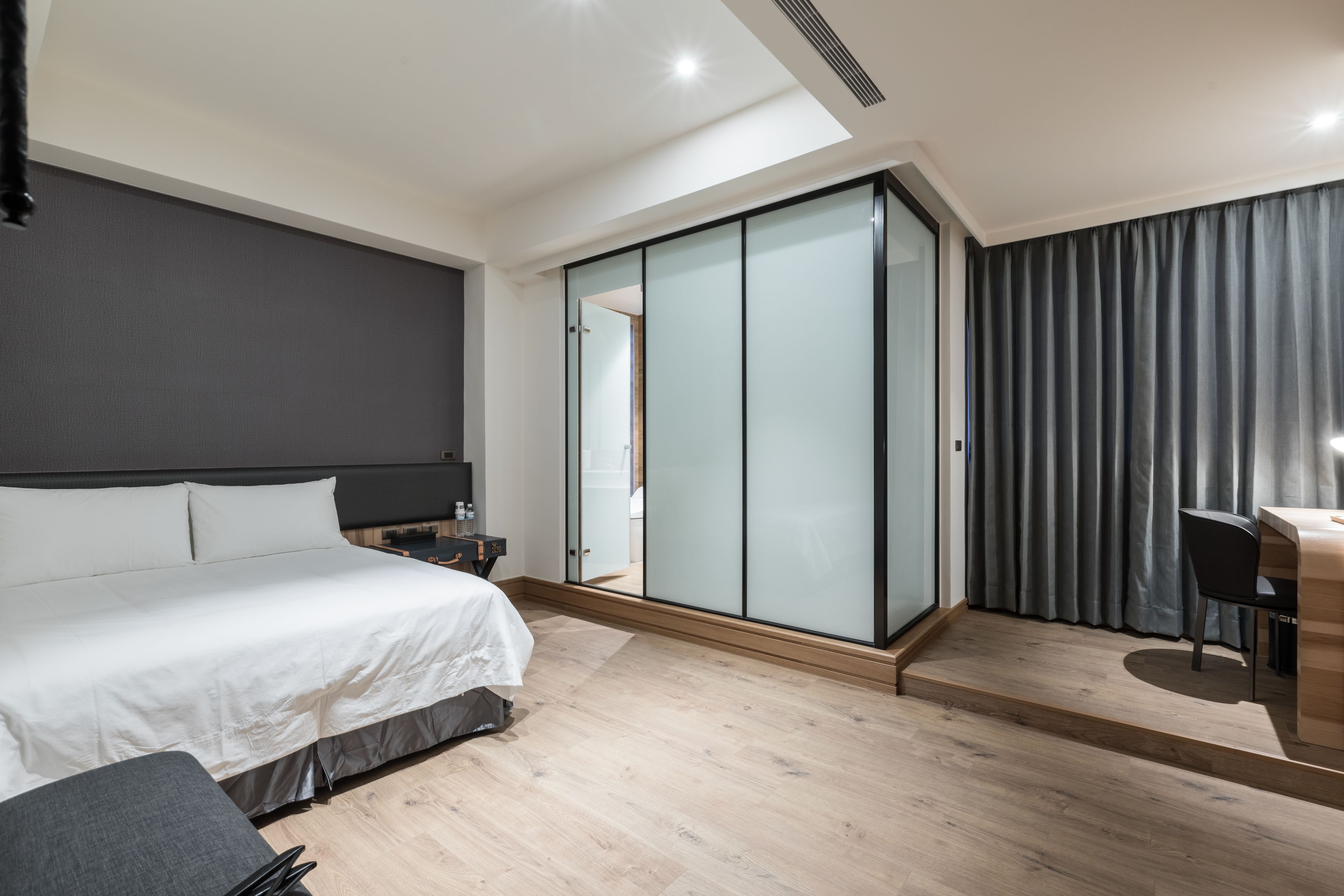 A modern hotel room with a large bed, a desk, and a sliding glass door closet.
