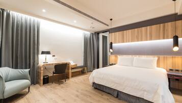 Una habitación de hotel moderna con piso de madera, una cama grande, un escritorio con silla y un sofá.