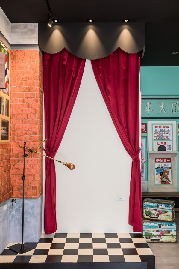 A room with a checkered floor, red curtains, a brick wall, and a poster on the wall. - Peach Blossom (Taitung)