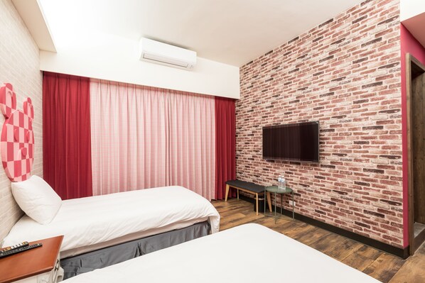 Habitación de hotel con dos camas, un televisor montado en una pared de ladrillo, una mesita pequeña y un banco.