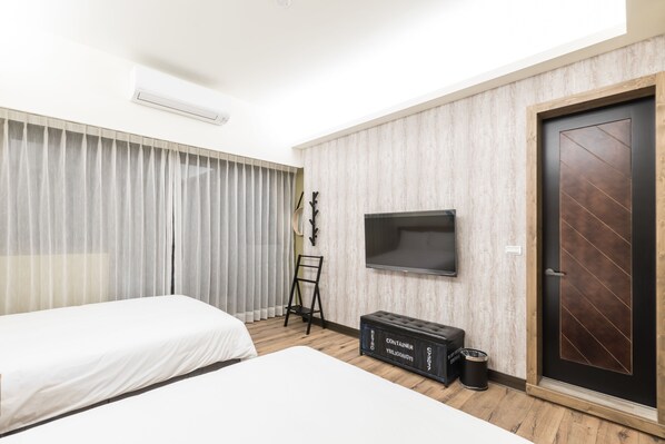 A hotel room with two beds, a TV, a wardrobe, and a small seating area. - Peach Blossom (Taitung)
