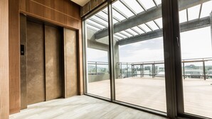 Un ascensor moderno con puerta de cristal, pared de paneles de madera y vista a una terraza en la azotea.