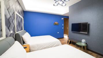 A hotel room with two beds, a TV mounted on the wall, a small table with water bottles, and a bench.