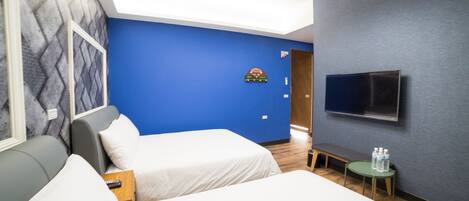 Ein Hotelzimmer mit zwei Betten, einem an der Wand montierten Fernseher, einem kleinen Tisch mit Wasserflaschen und einer Bank.