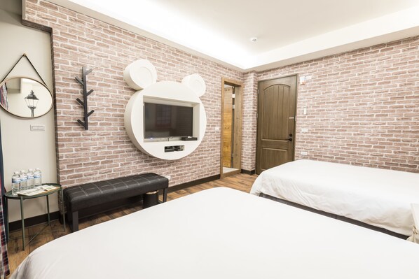 Habitación de hotel con pared de ladrillo, un espejo redondo, televisor de pantalla plana montado en la pared, un banco, dos camas y una puerta de madera.