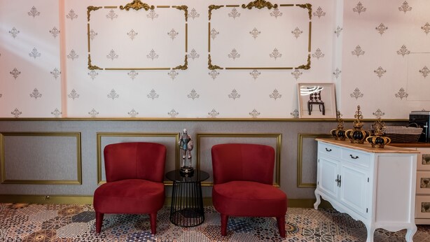 A room with two red chairs, a small table with a statue, a white cabinet with decorative items, and patterned wallpaper. - Peach Blossom (Taitung)