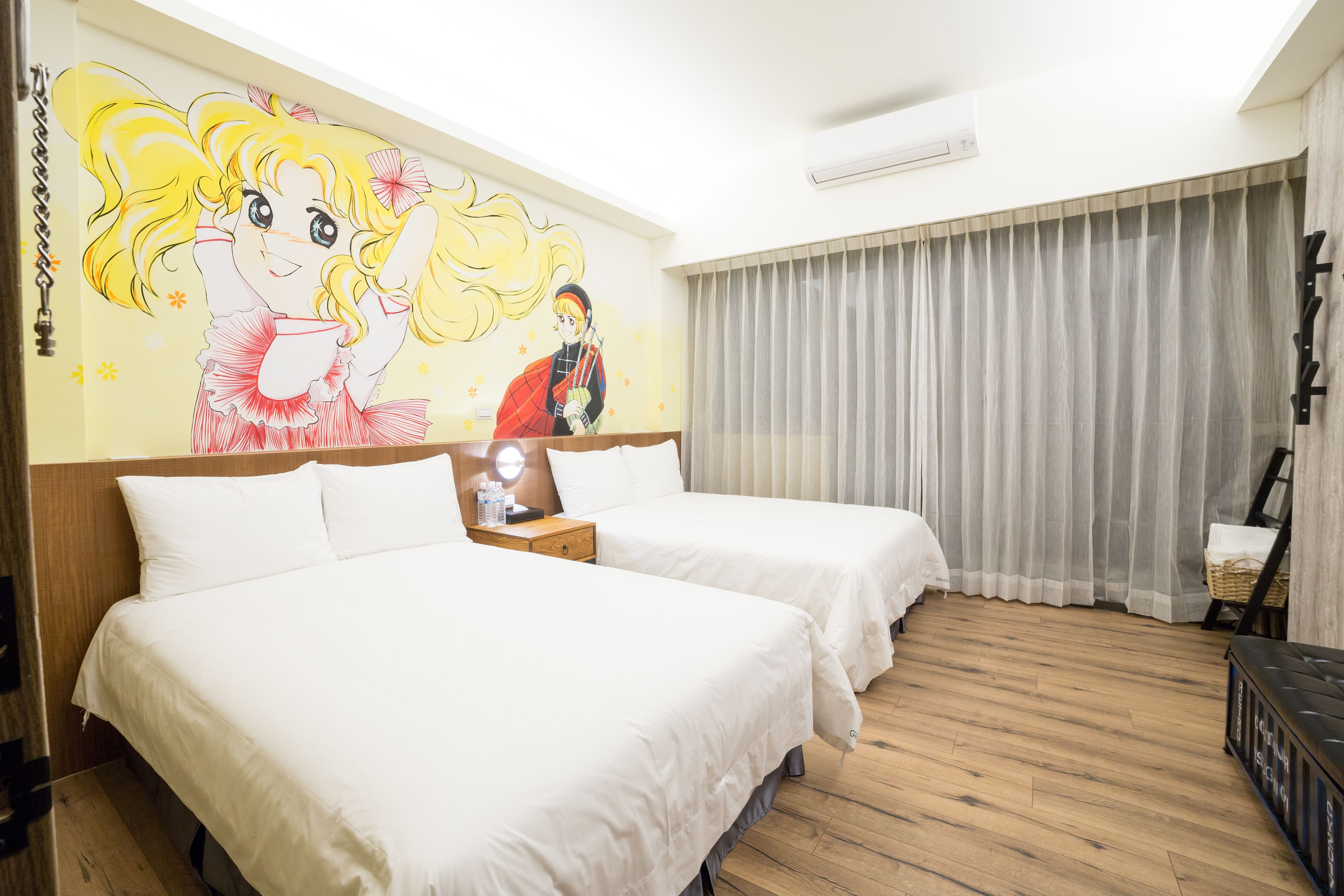 A hotel room with two beds, a mural on the wall, a wooden floor, and a window with curtains.