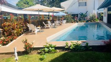 Uma área de piscina com espreguiçadeiras e guarda-sóis, rodeada por vegetação exuberante e plantas floridas.
