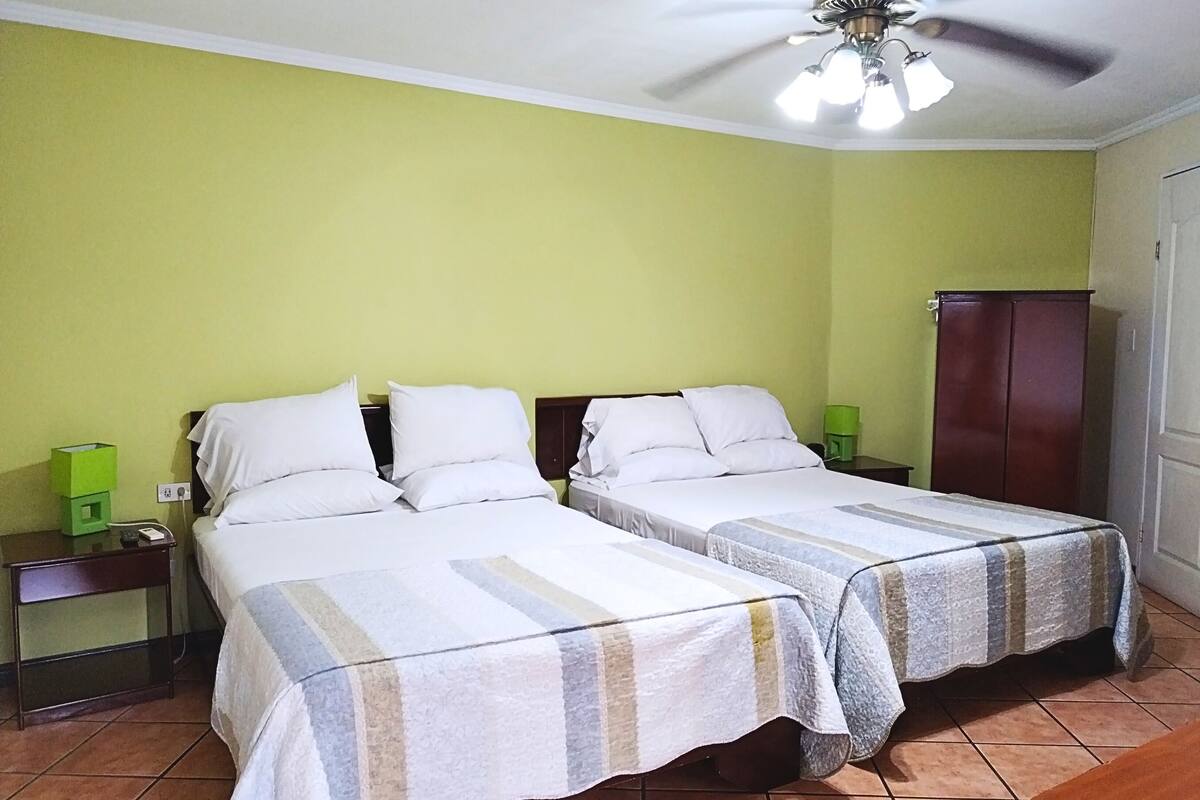A hotel room with two beds, a ceiling fan, a green wall, and a wooden wardrobe.