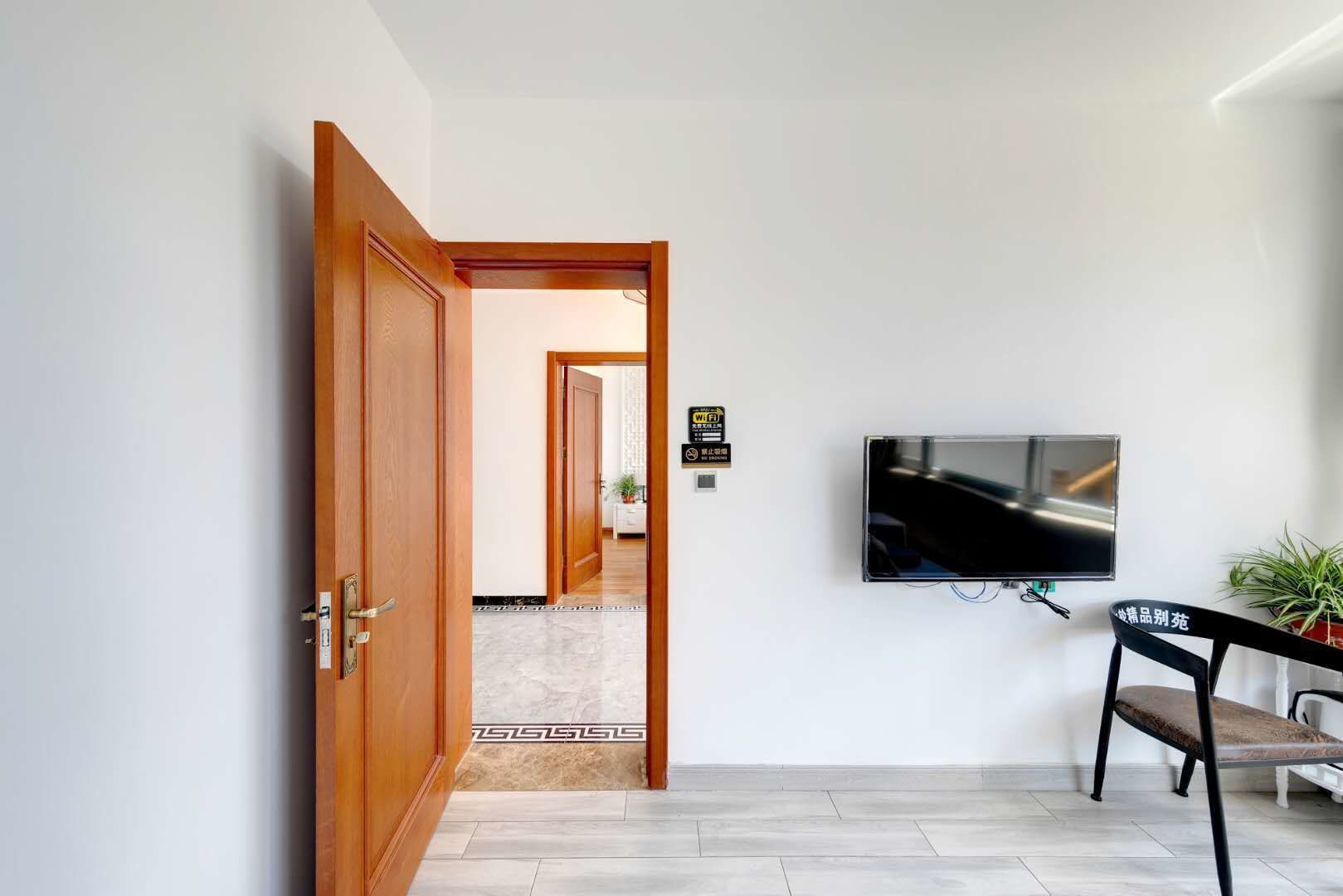 Un couloir avec une porte en bois, un téléviseur à écran plat fixé au mur et une chaise avec un coussin.
