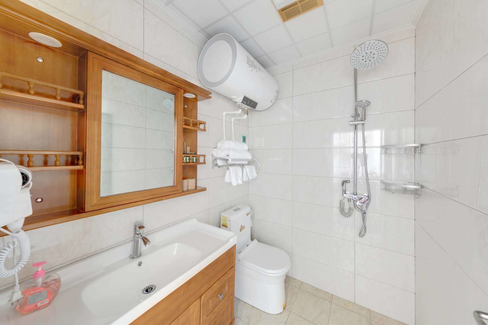 Un baño moderno con un espejo grande, un lavamanos con dispensador de jabón, inodoro y ducha con cabezal de ducha de mano.