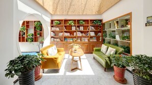 Un salon spacieux avec un plafond haut, des étagères en bois, un canapé jaune, un canapé vert et des plantes en pot.