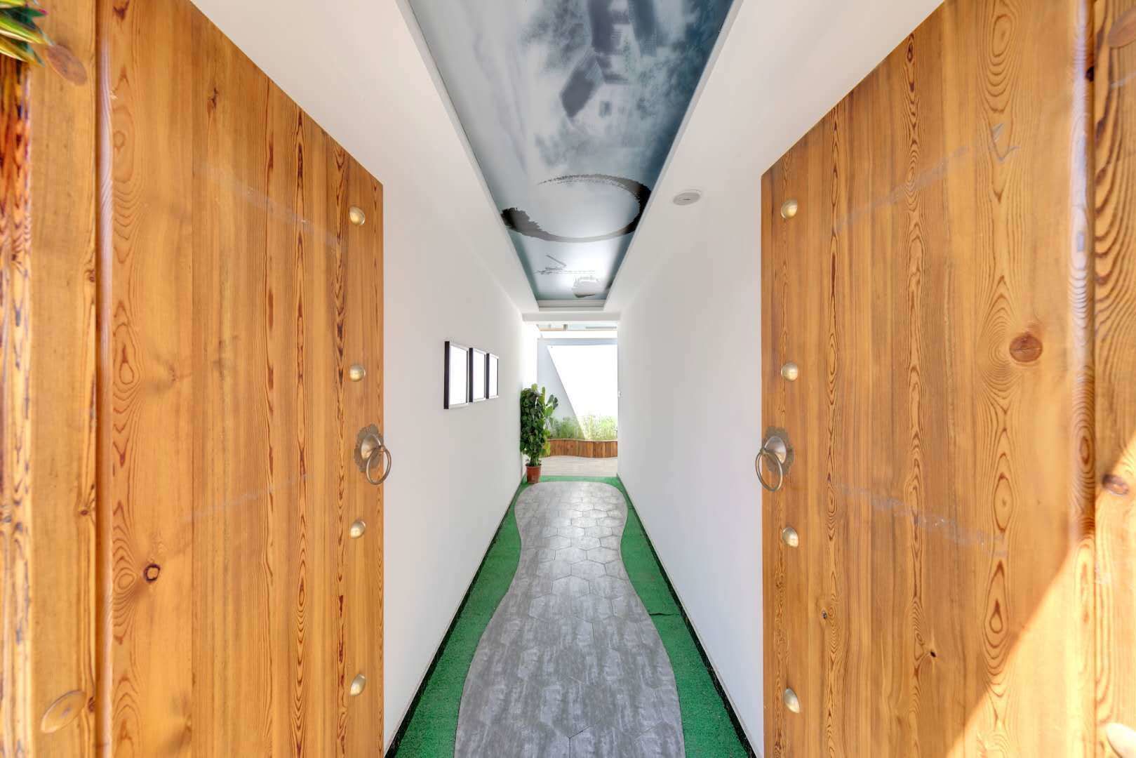 Un pasillo con puertas de madera, alfombra verde y un mural en el techo.