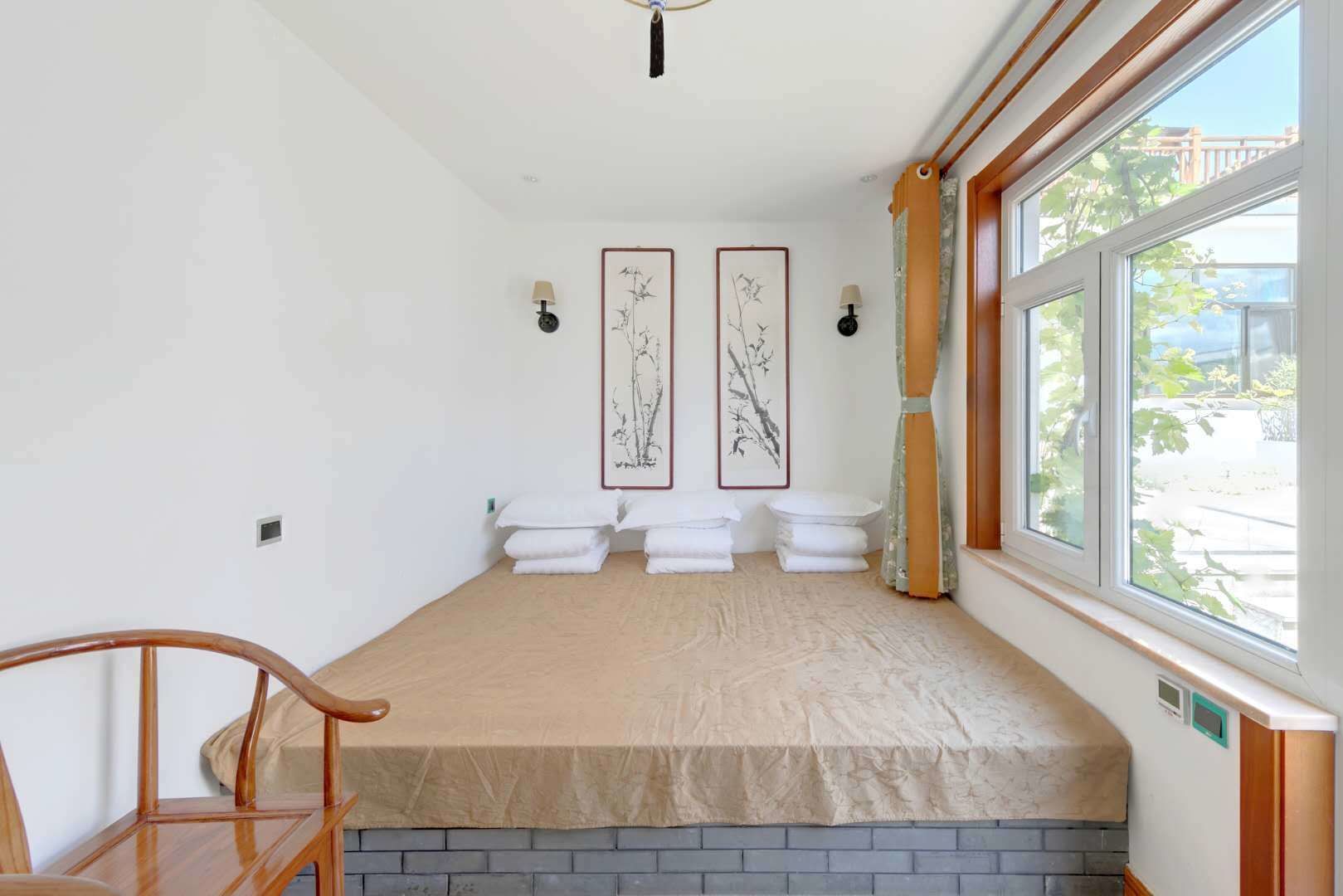 A room with a wooden bench, two framed artworks on the wall, and a window with a view of greenery.