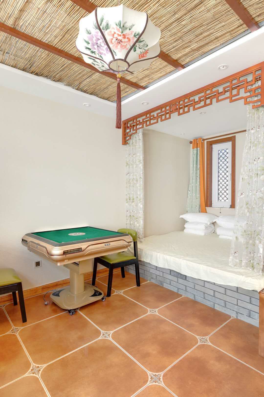 A room with a pool table, a green cushioned chair, a bed with white bedding, and a decorative ceiling fan.