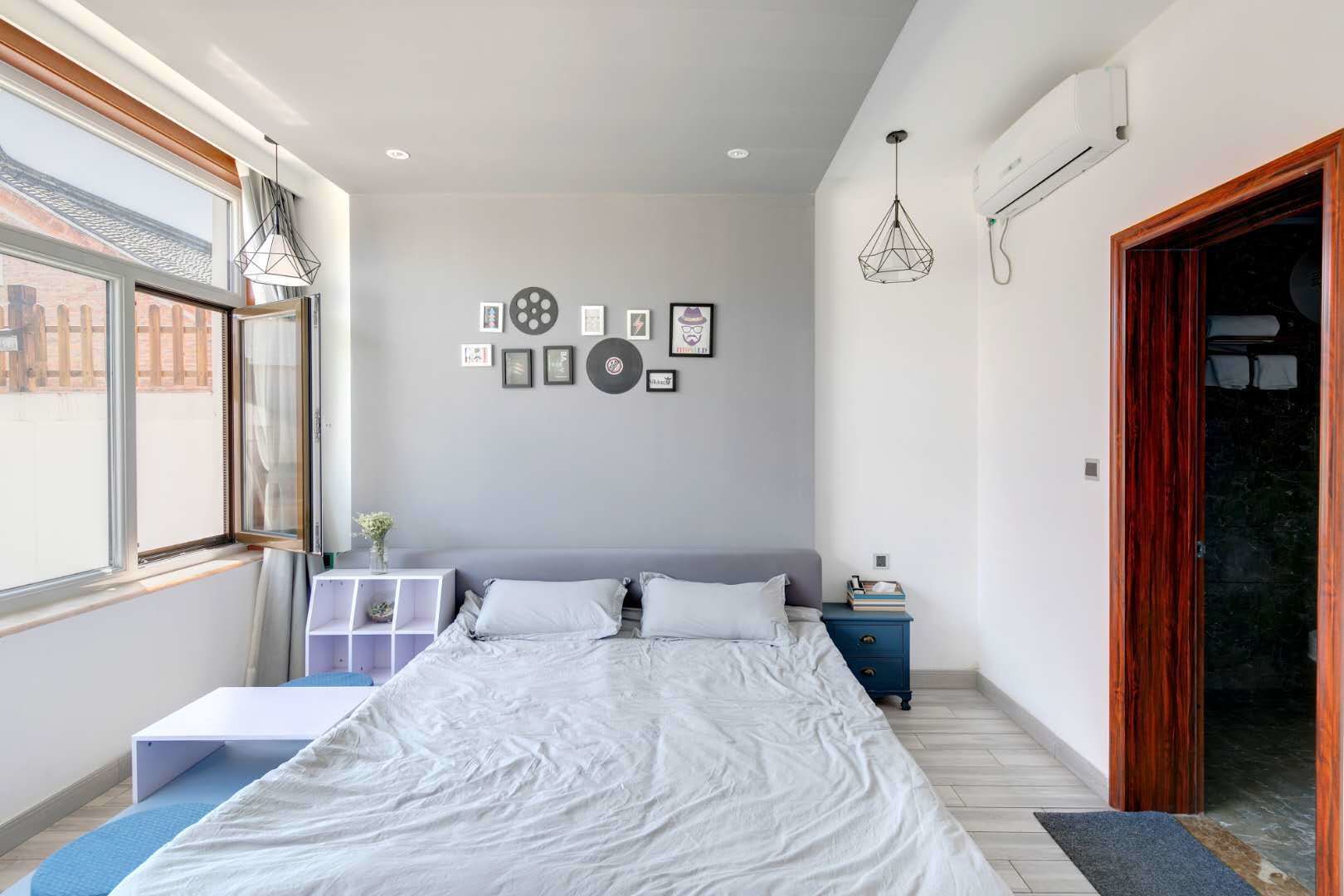 A bedroom with a large bed, a bedside table, a wardrobe, and a window with a view of a brick building.