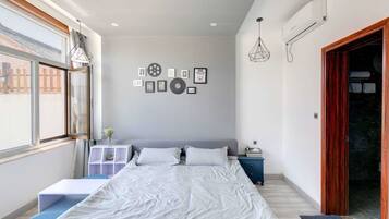 A bedroom with a large bed, a bedside table, a wardrobe, and a window with a view of a brick building.