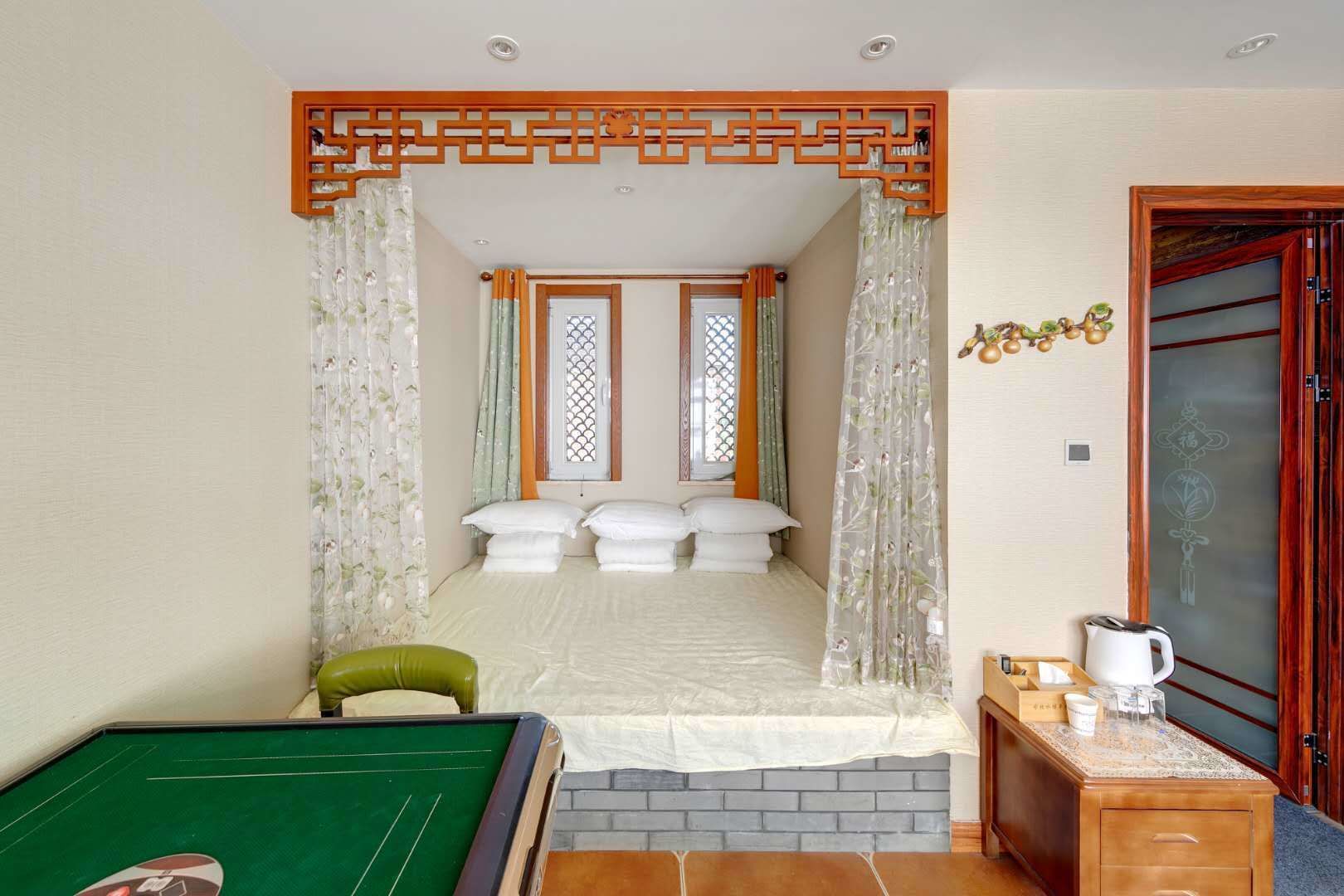 A room with a bed, a green pool table, a wooden cabinet with a kettle, and a door with decorative elements.