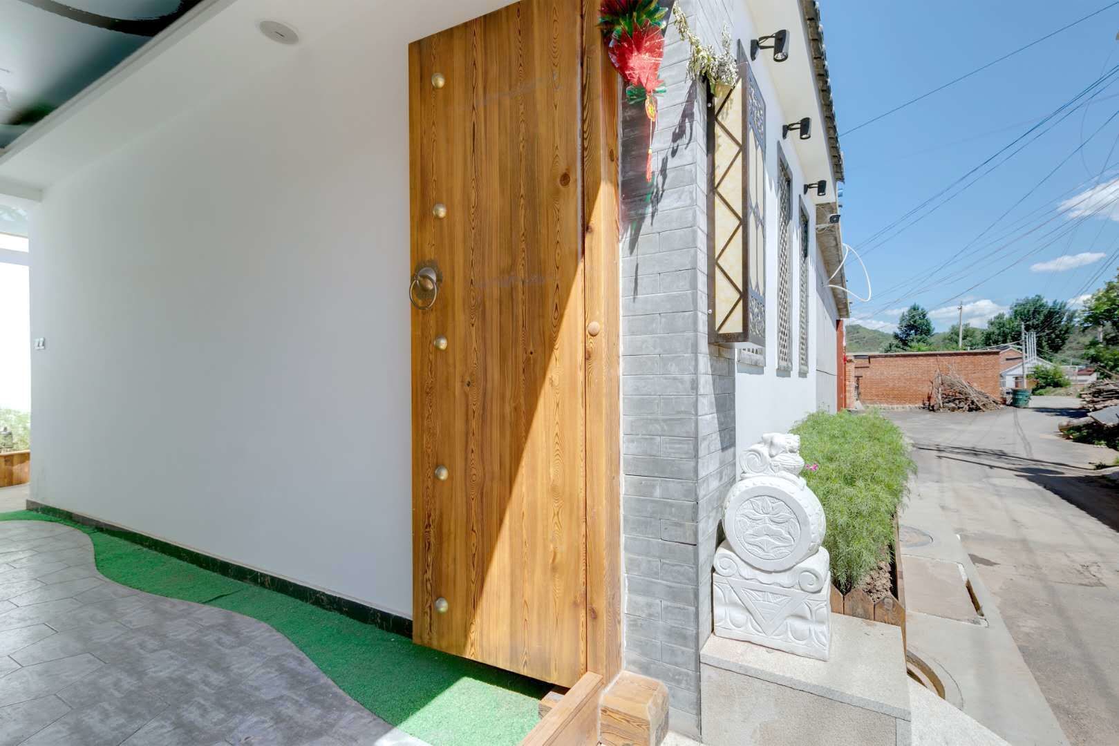 Un edificio moderno con puerta de madera, un pequeño jardín con una estatua y un acceso pavimentado.