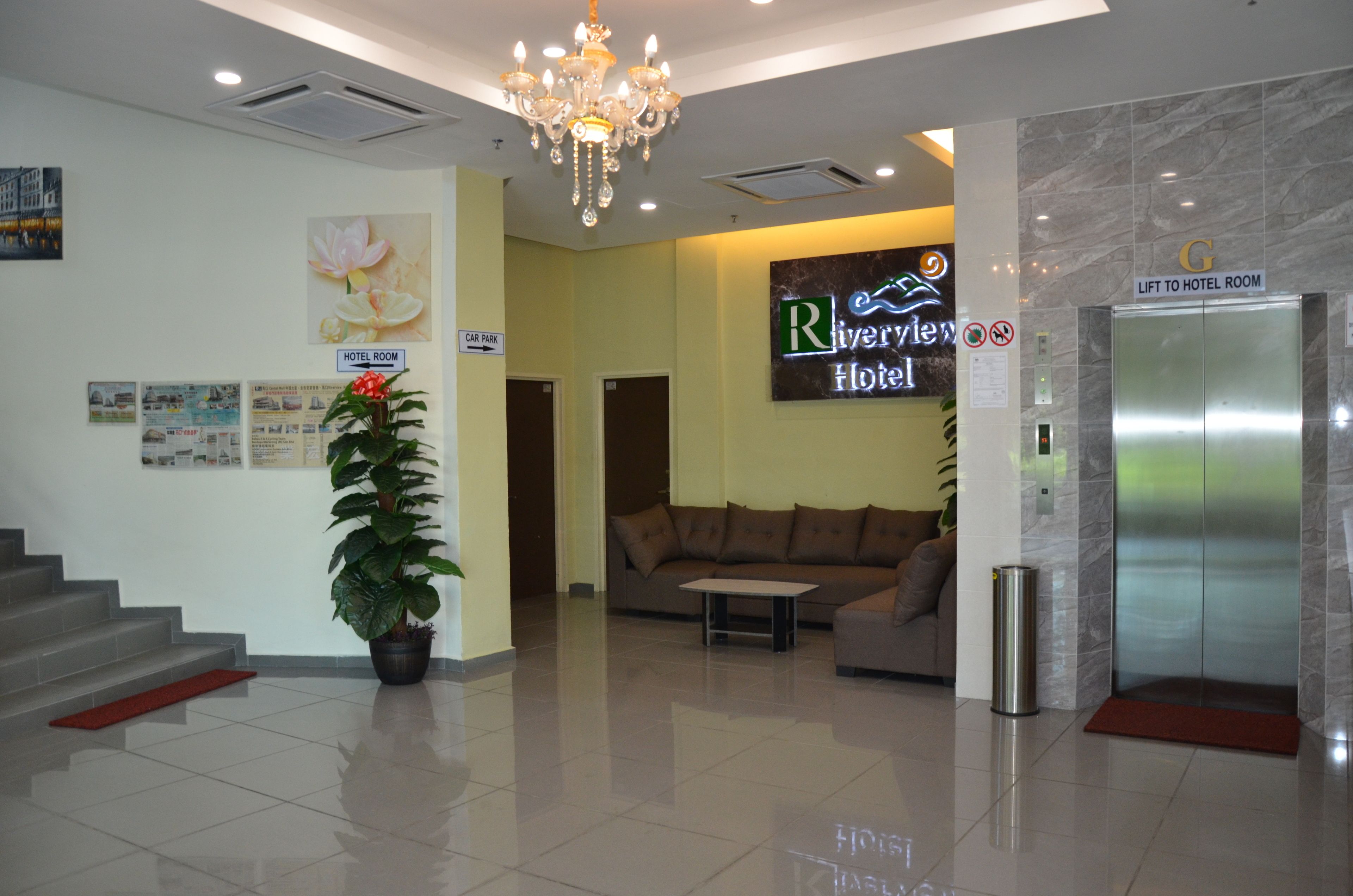A hotel lobby with a reception desk, a sofa, a chandelier, a potted plant, and an elevator.