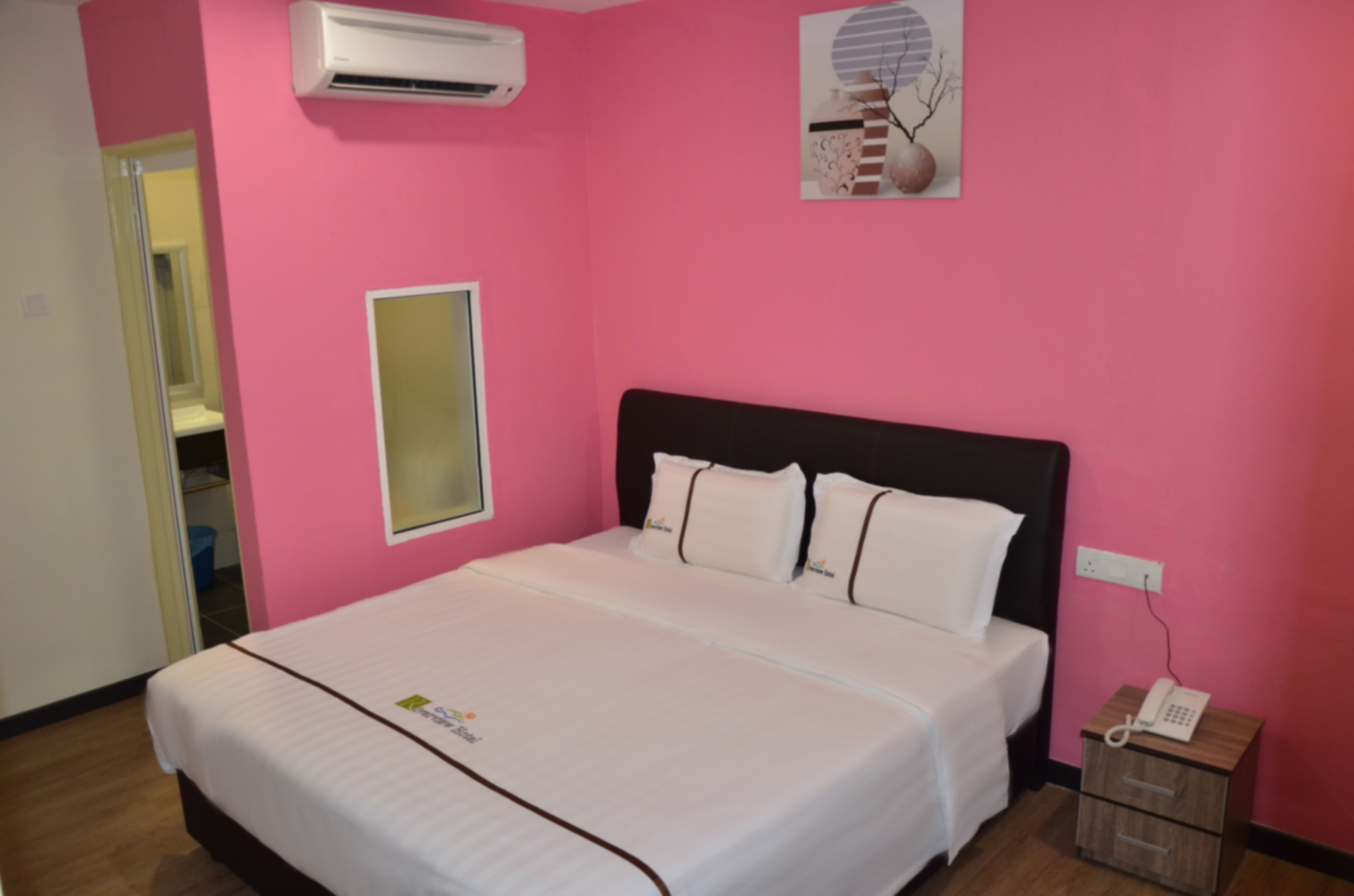 A hotel room with a large bed, a bedside telephone, and a wall-mounted air conditioner.