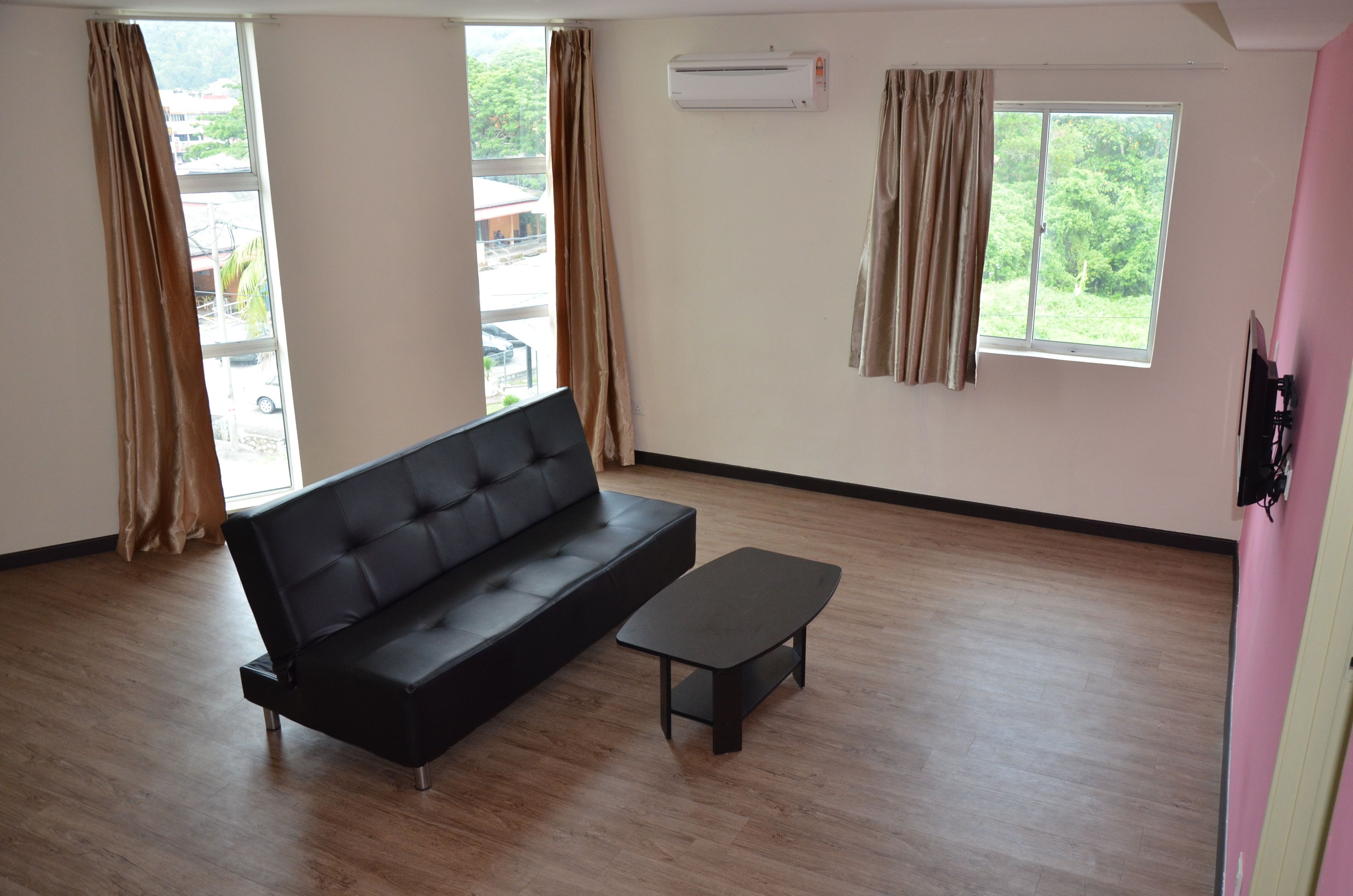 A room with a black sofa and a small table, large windows with curtains, an air conditioning unit, and a view of the outside.