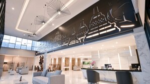 A modern hotel lobby with a reception desk, seating area, and decorative wall art. - Grand Senyum Hotel (Yogyakarta)