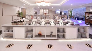 A modern hotel lobby with a central buffet area, marble flooring, and a large chandelier. - Grand Senyum Hotel (Yogyakarta)